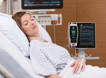 Woman sleeping in hospital bed monitored by Masimo Root device.